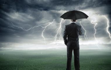 A man in the suit standing in the storm with an umbrella