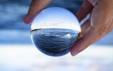 A hand holding a glass ball and looking at seaside