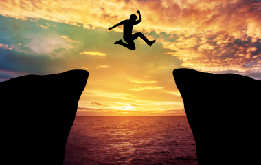A man jumping over cliff with sunset in background