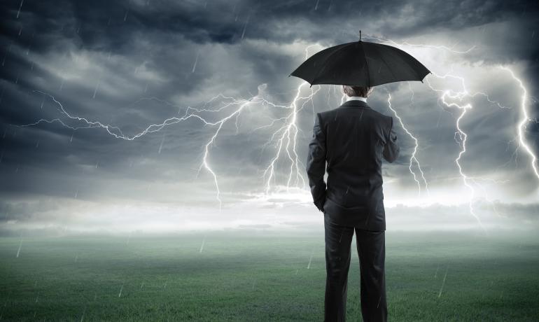 A man in the suit standing in the storm with an umbrella