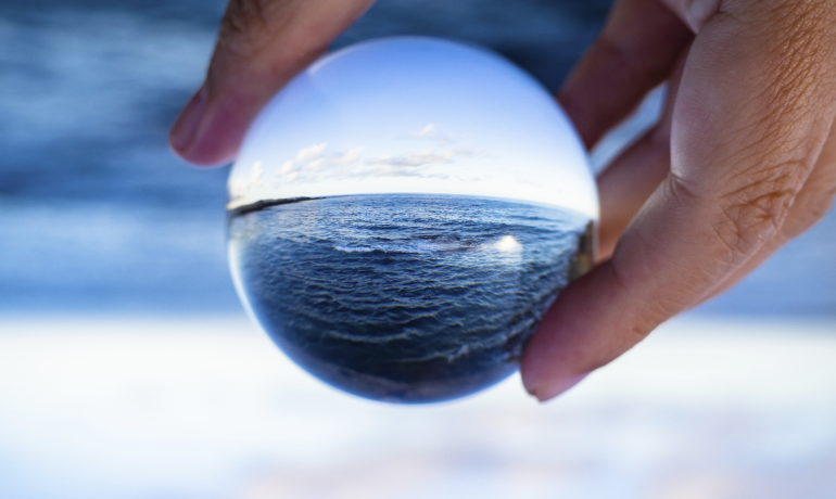 A hand holding a glass ball and looking at seaside